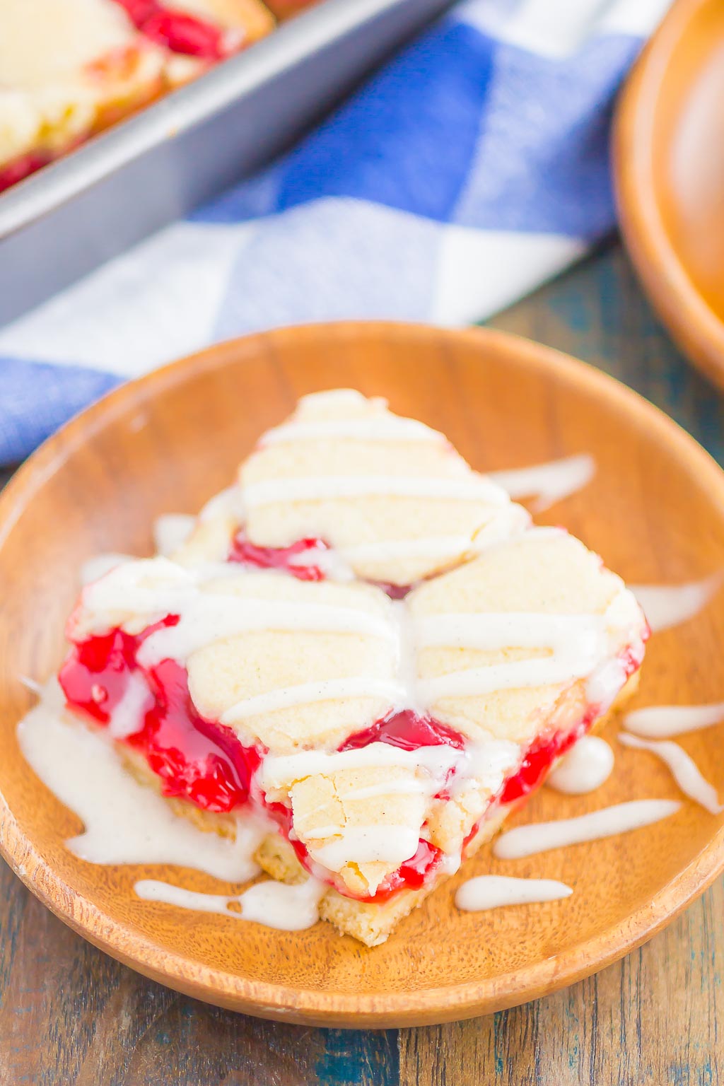 A cherry pie bar topped with glaze on a small wooden plate. 