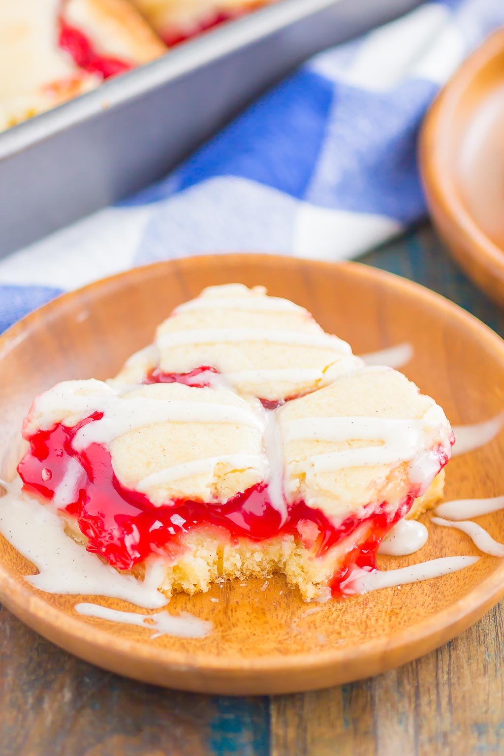 A glazed cherry pie bar on a small wooden plate. A bite is missing. 