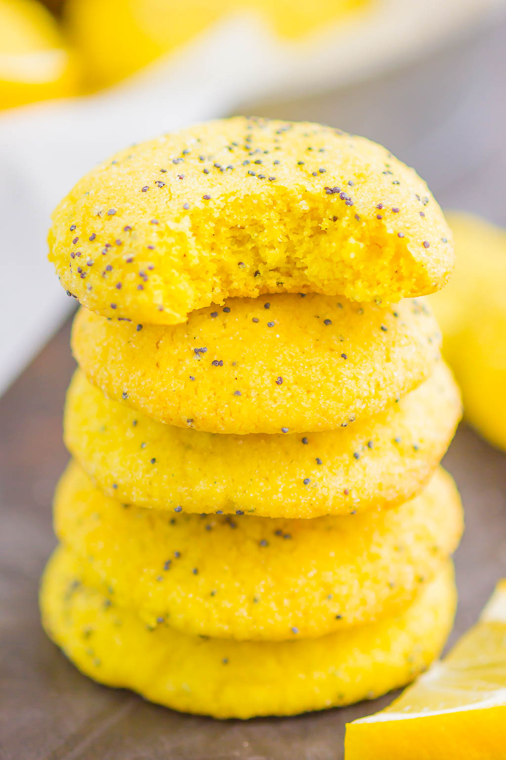 A stack of five lemon poppy seed cookies. The top cookie has a bite missing. 