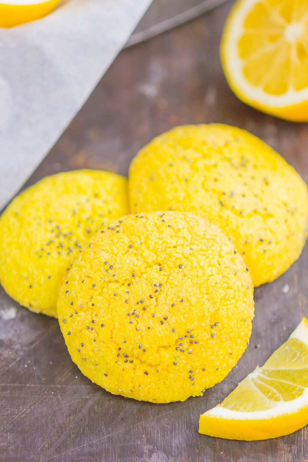 A group of three soft lemon cookies surrounded by lemon halves and wedges. 