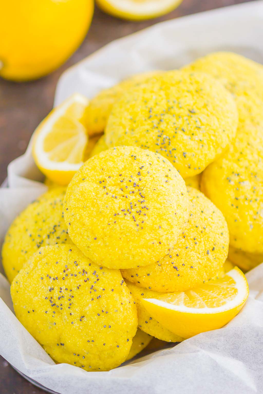Lemon poppy seed cookies piled in a metal basket with lemon wedges. 