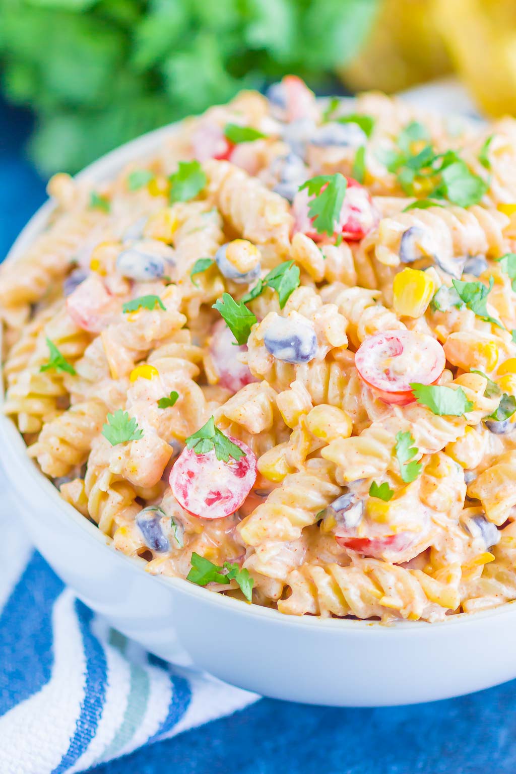 A serving bowl filled with taco pasta salad. Fresh cilantro rests in the background. 