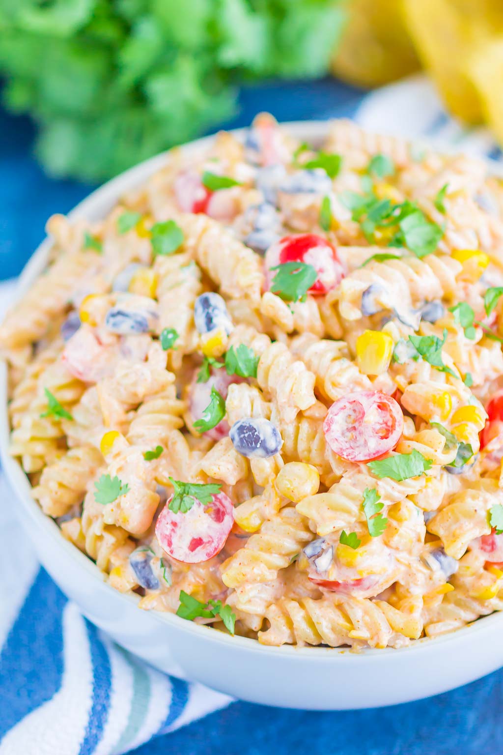 A serving bowl filled with taco pasta salad. Fresh cilantro rests in the background. 