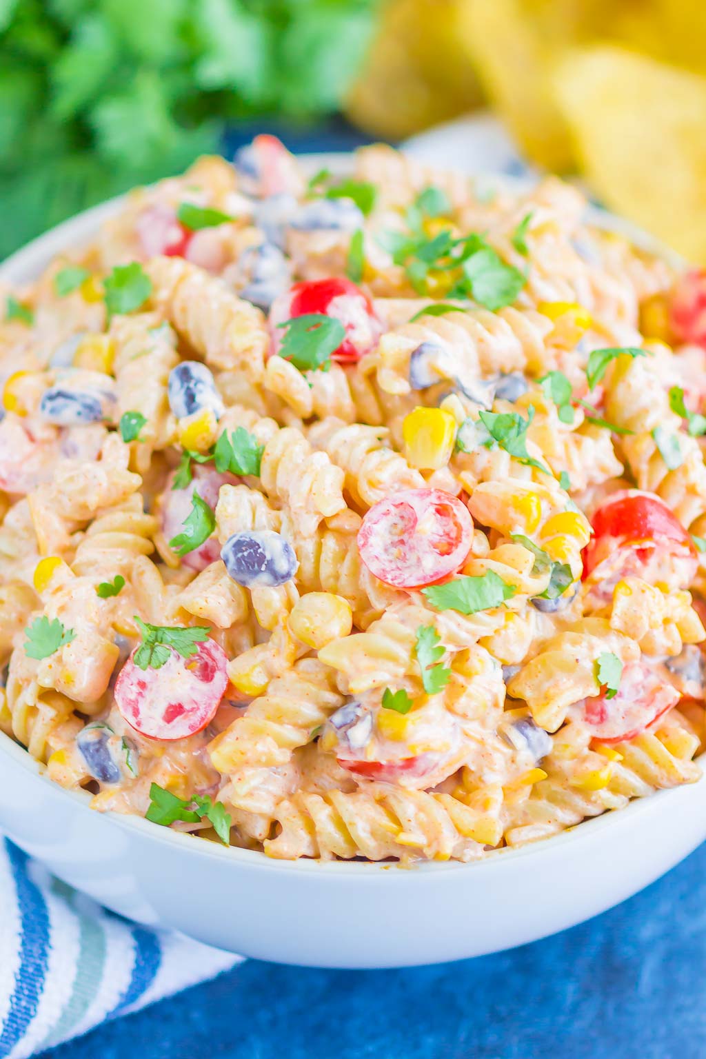 A serving bowl filled with taco pasta salad. Fresh cilantro rests in the background. 