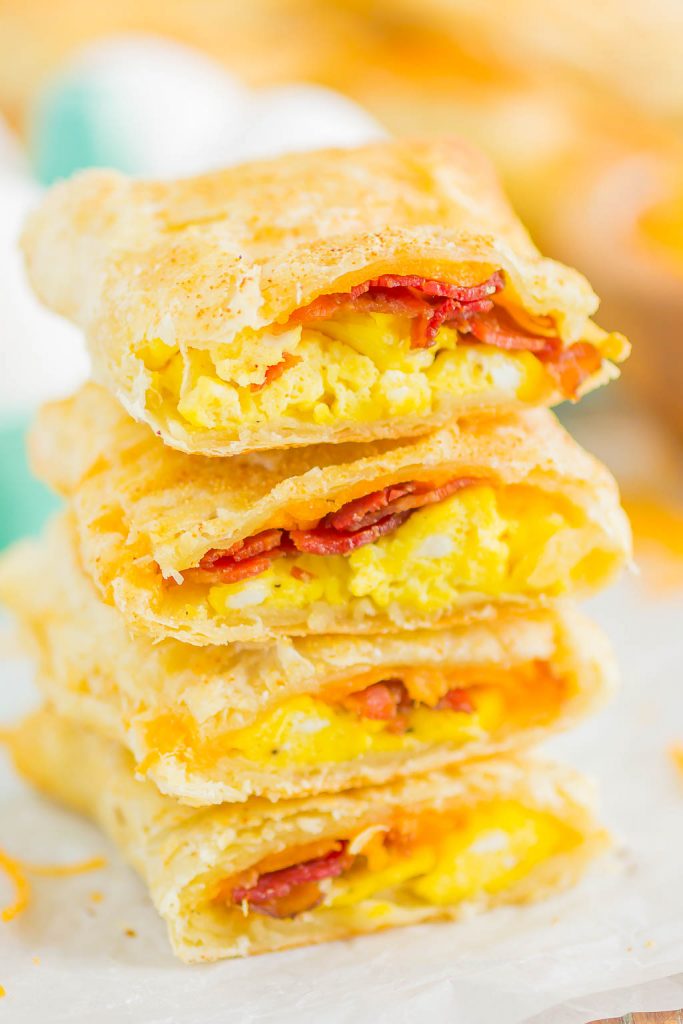 A stack of homemade breakfast hot pockets filled with scrambled eggs, bacon, and melted cheese, with flaky golden-brown crusts, shown on a piece of parchment paper.