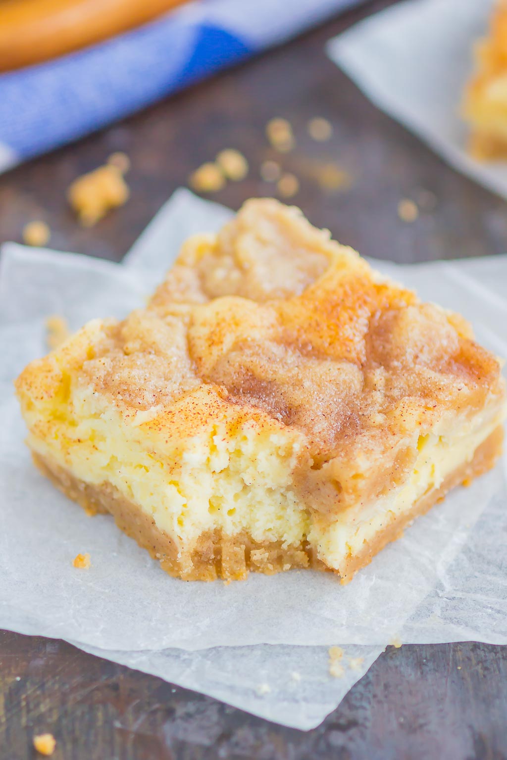 Snickerdoodle Cheesecake Bar with a bite missing, on a square of parchment paper. 