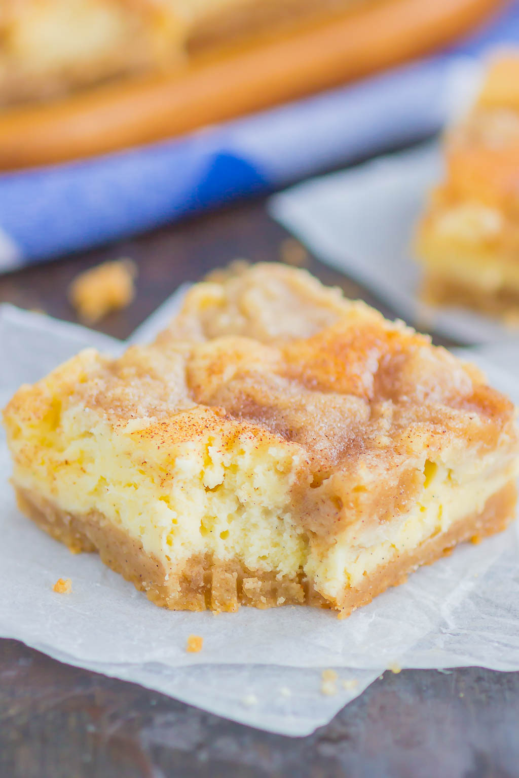 A Snickerdoodle Cheesecake Bar with a bite missing on a square of parchment paper. 