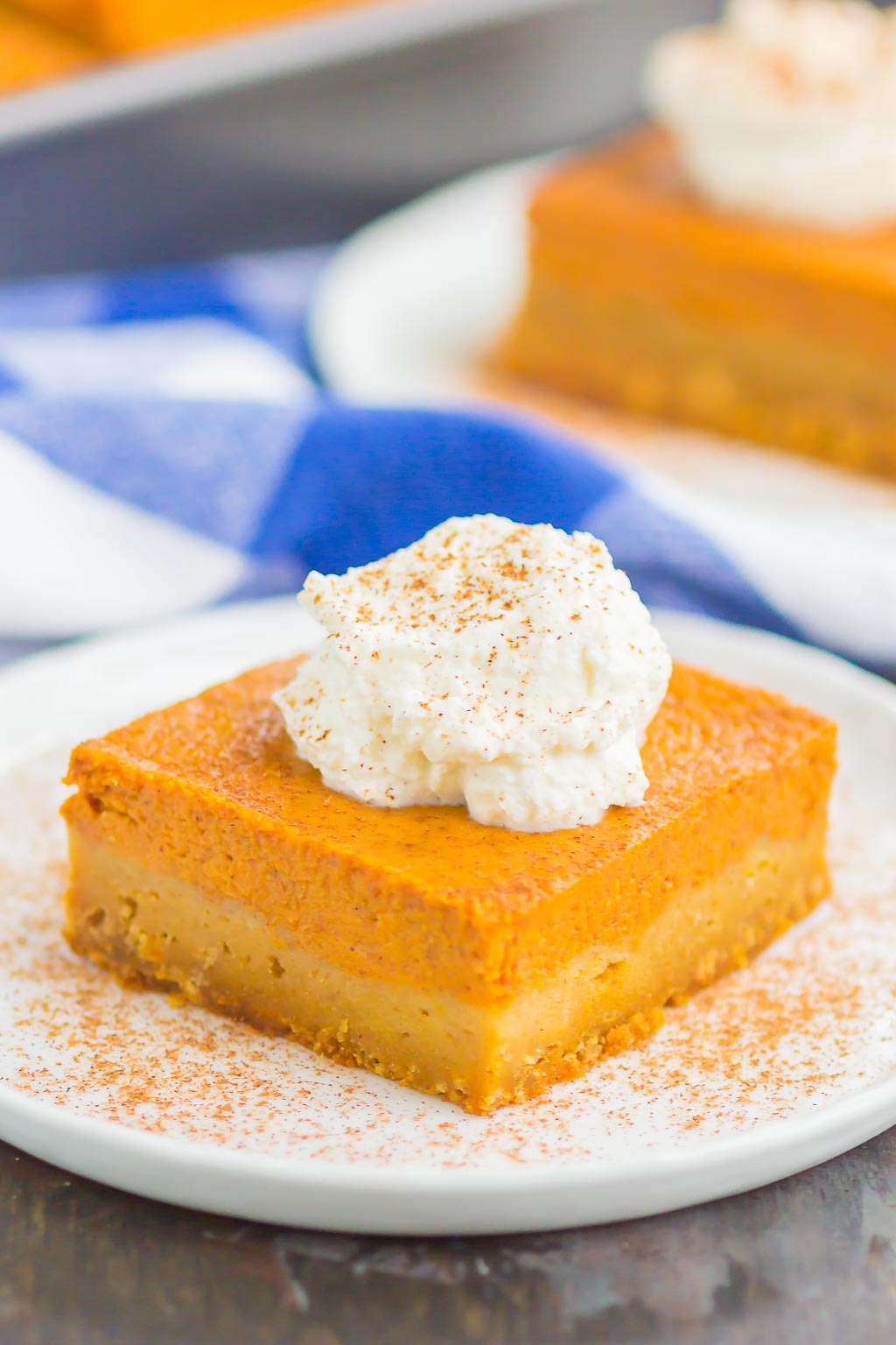 A pumpkin pie square garnished with whipped cream on a plate. 