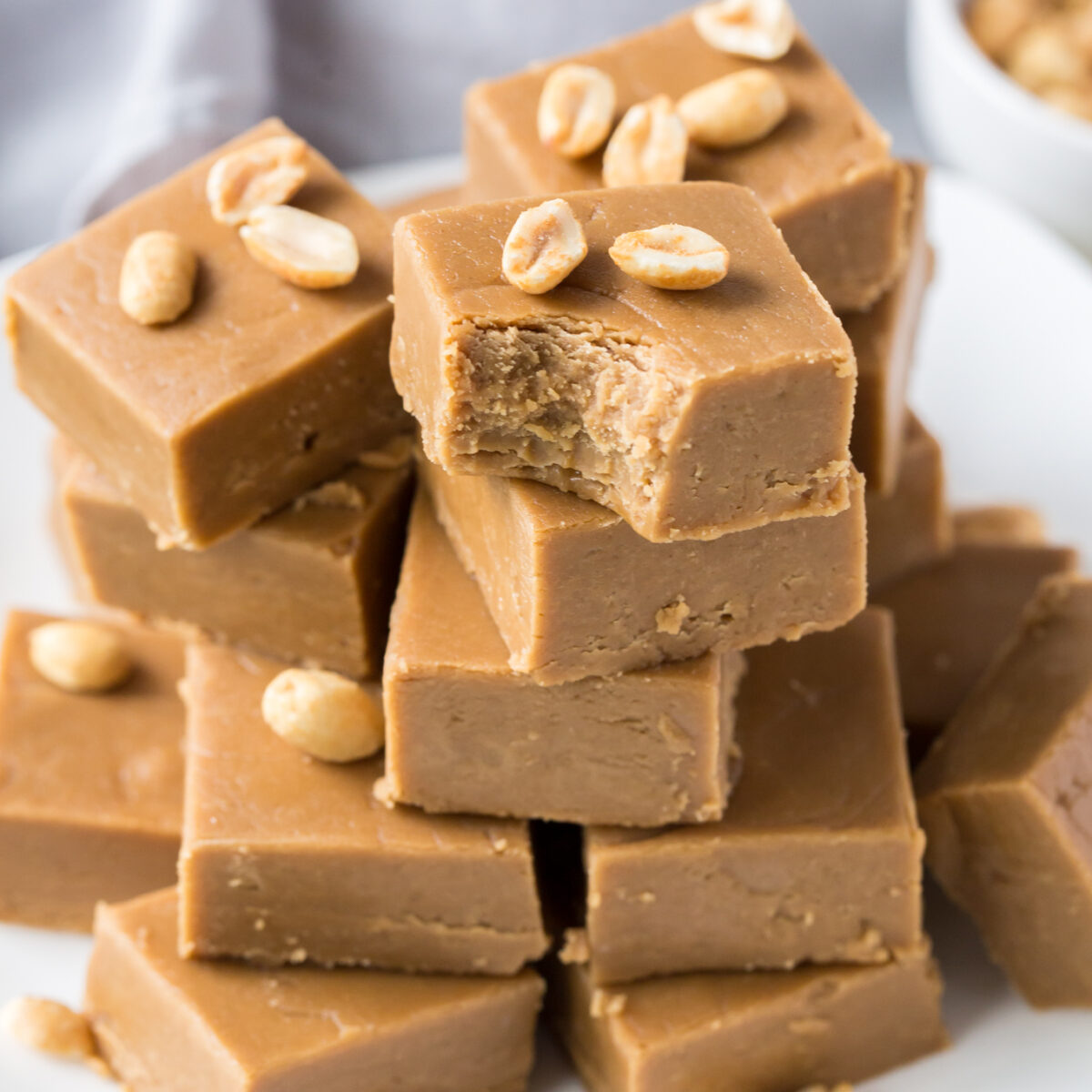 the best Peanut Butter Fudge, piled high on a white plate and garnished with peanuts