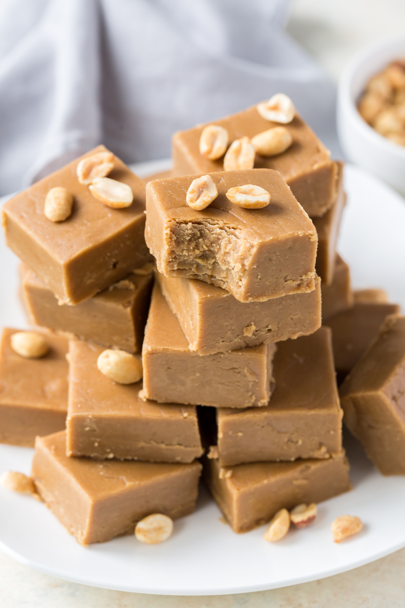 the best Peanut Butter Fudge, piled high on a white plate and garnished with peanuts 