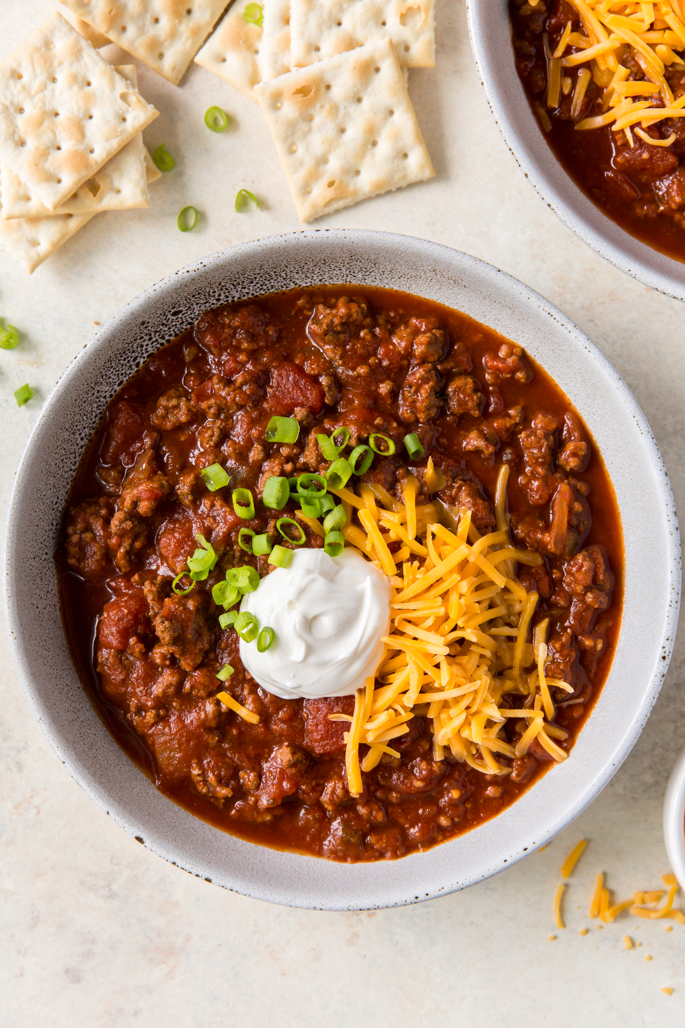 A large bowl of bean-free chili topped with chives, cheddar cheese, sour cream and crackers.