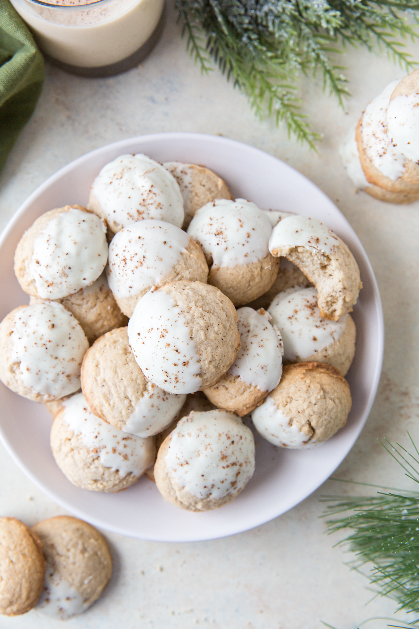 overhead view of White Chocolate Eggnog Cookies on a white plate surrounded by greenery