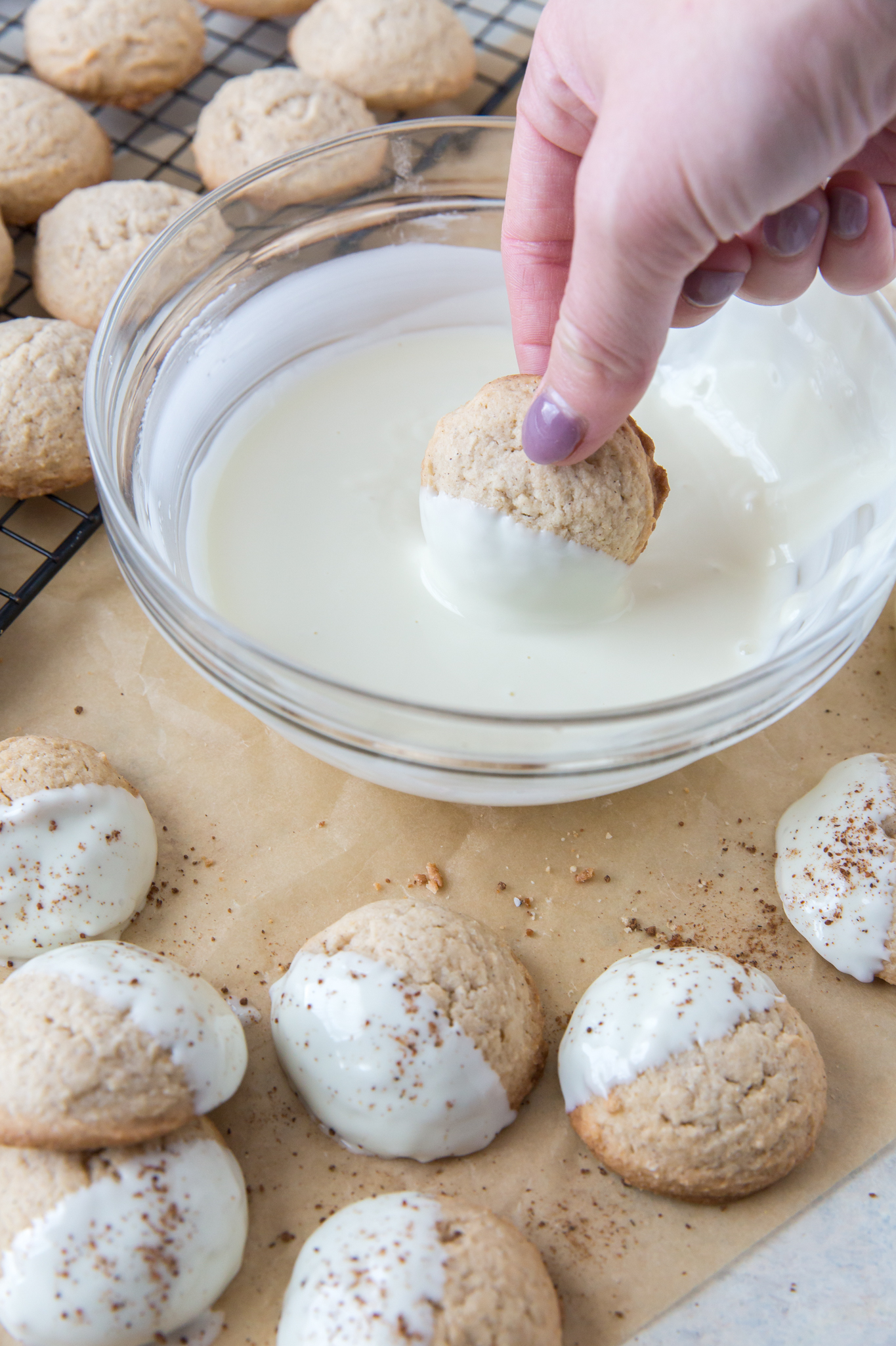 An eggnog cookie being dipped into a bowl of melted white chocolate 