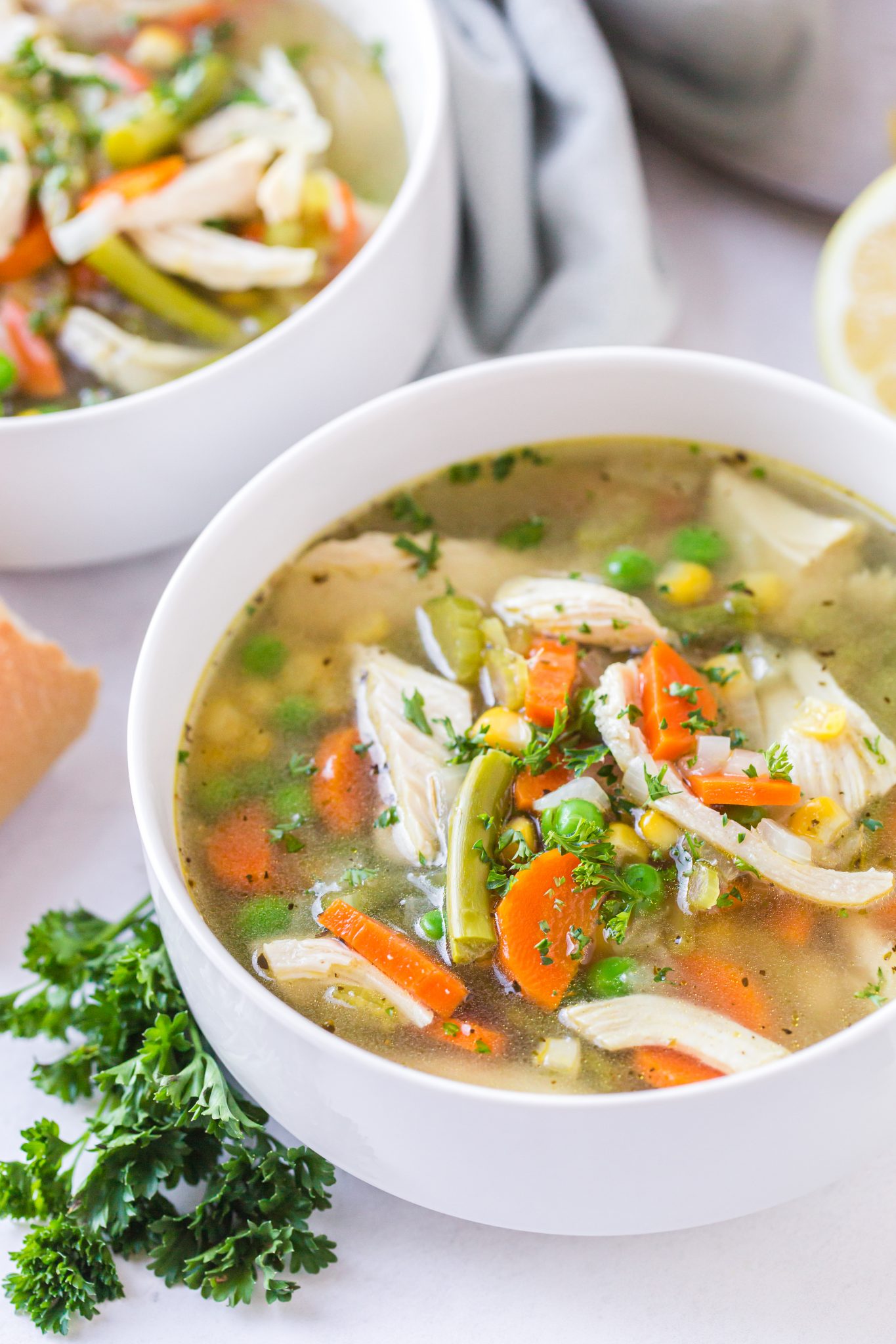 Two bowls of chicken asparagus soup with a sprig of fresh parsley on the side