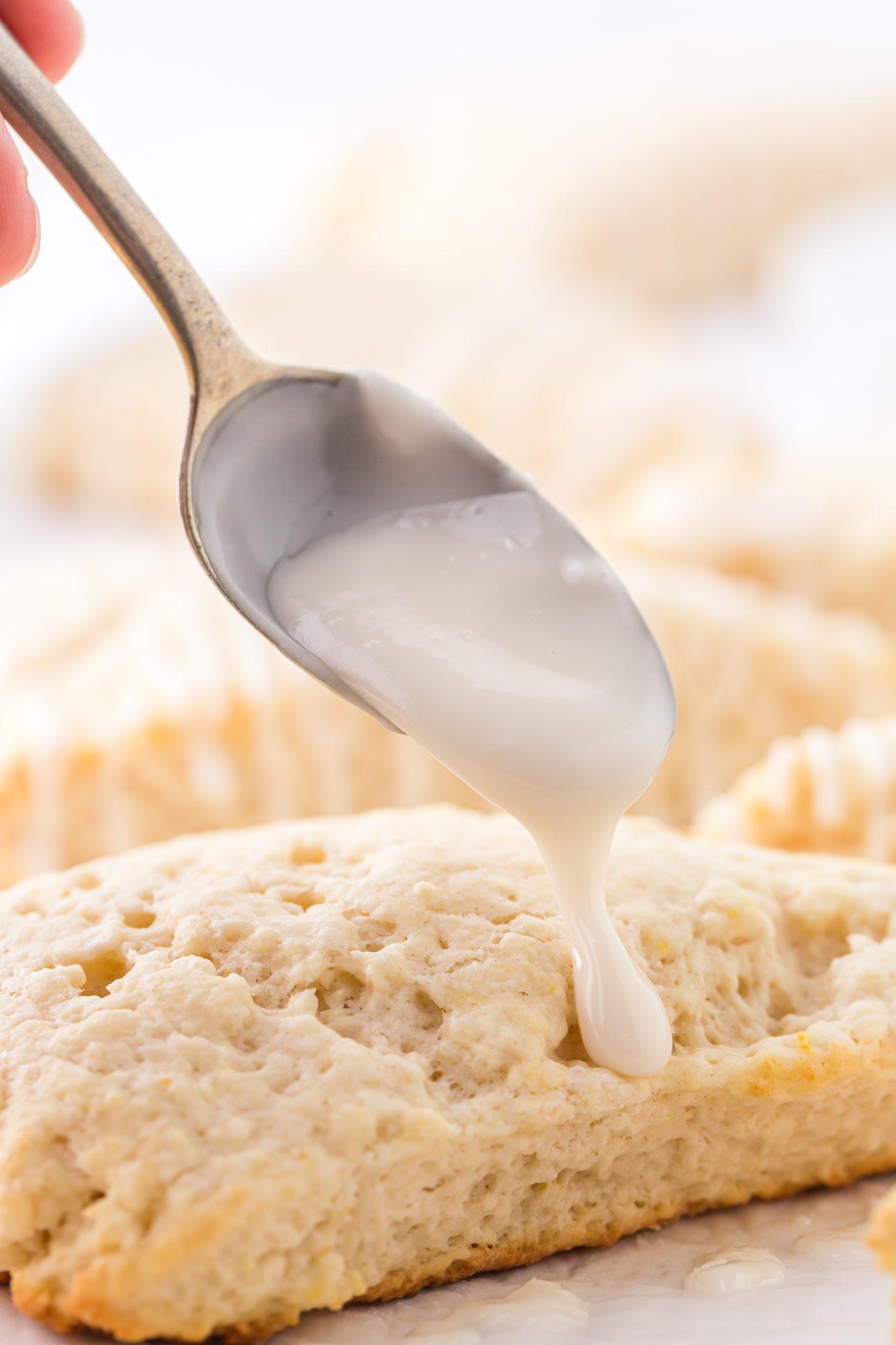 A close up view of a lemon scone being topped with lemon glaze.
