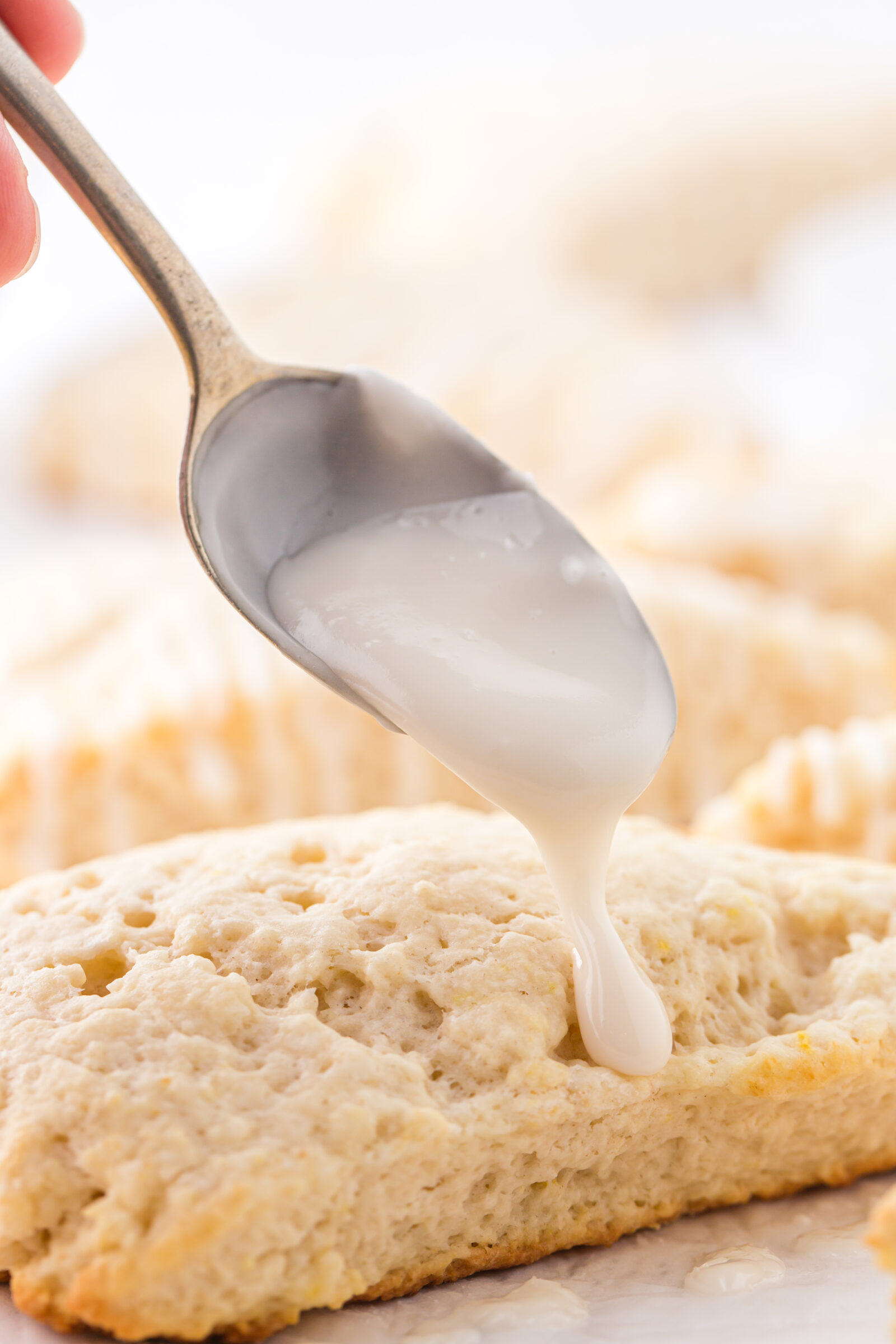 A close up view of a lemon scone being topped with lemon glaze. 