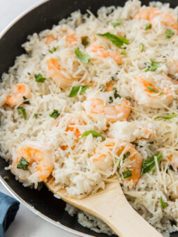 A skillet filled with creamy shrimp and rice, cooked to perfection with shredded cheese and fresh herbs, as a wooden spoon scoops up the delicious mixture.