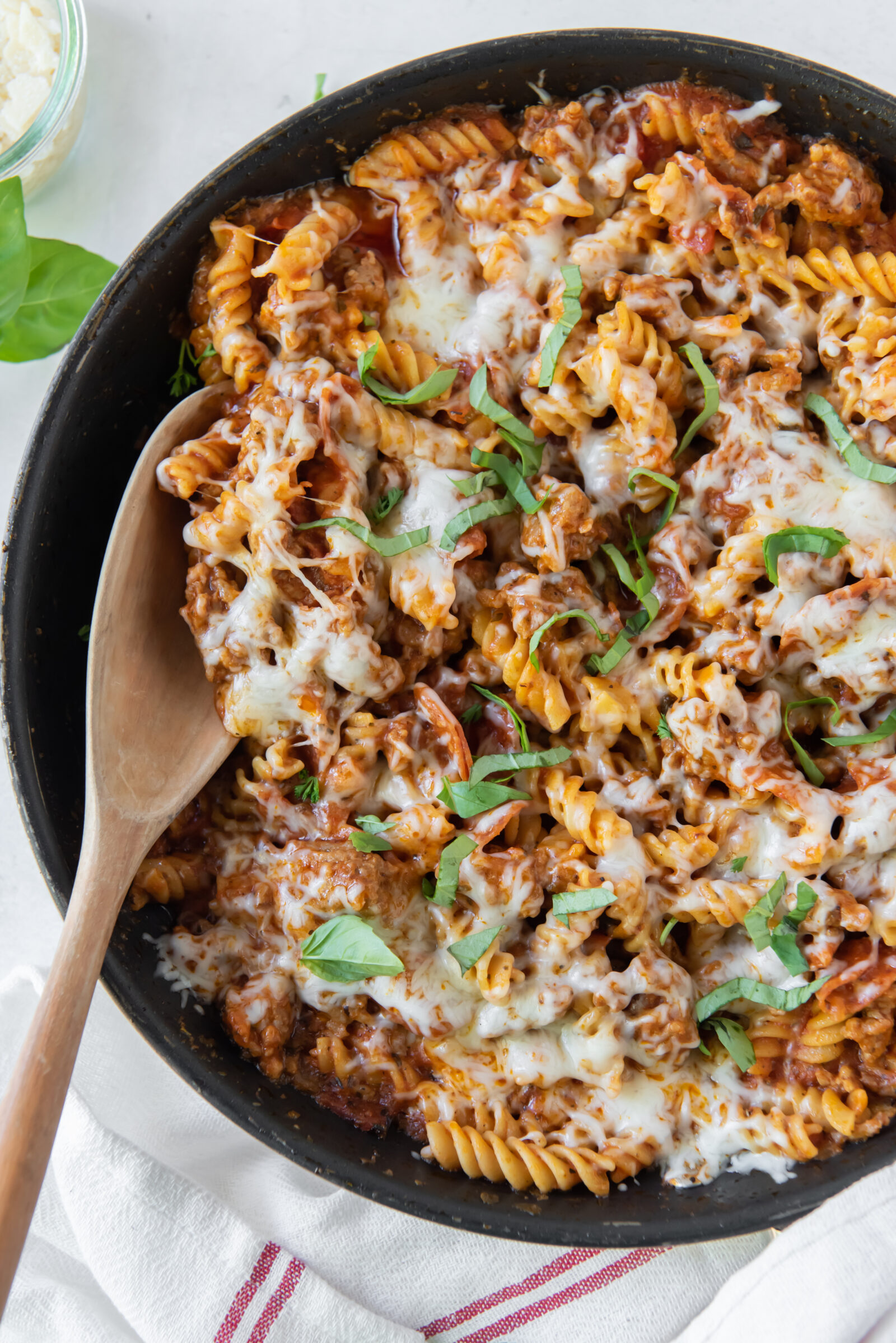 top view of pizza pasta casserole in a black pan with a wooden spoon