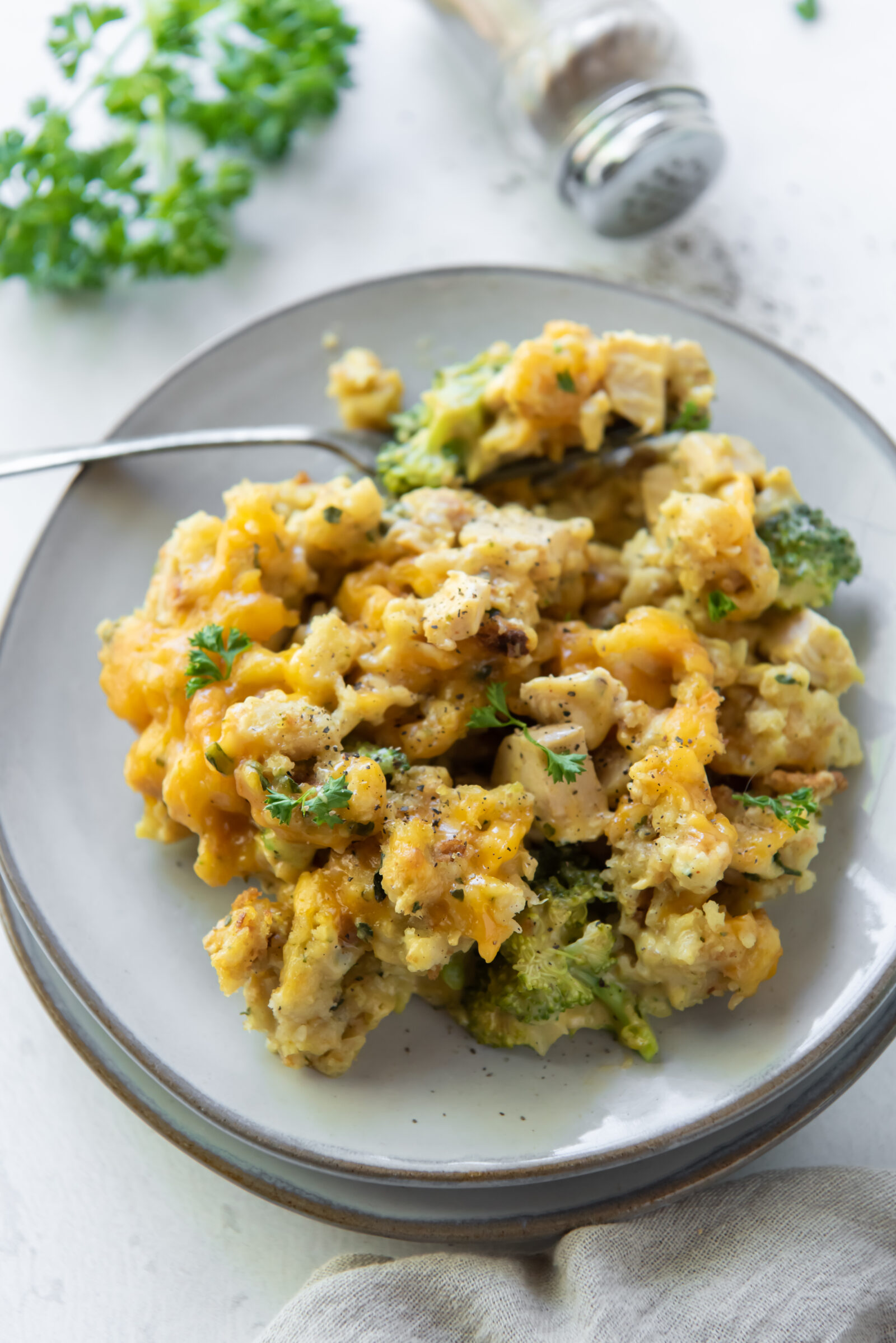 A portion of stuffing, broccoli and cheese casserole on a white plate with a fork. 