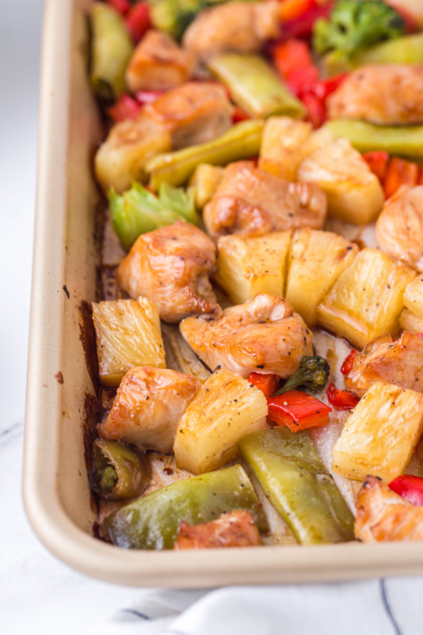 A sheet pan filled with pineapple teriyaki chicken pieces, pineapple chunks, red bell peppers, green bell peppers, and broccoli, all lightly browned and glazed.