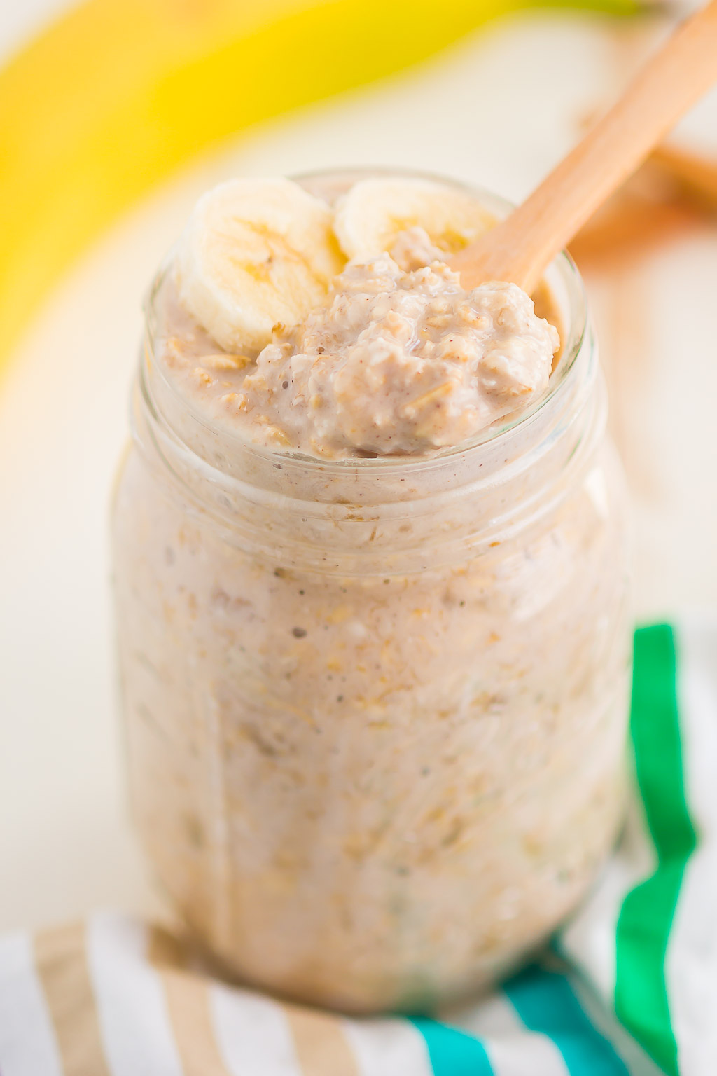 A wooden spoon digging into a jar of banana bread overnight oats. 