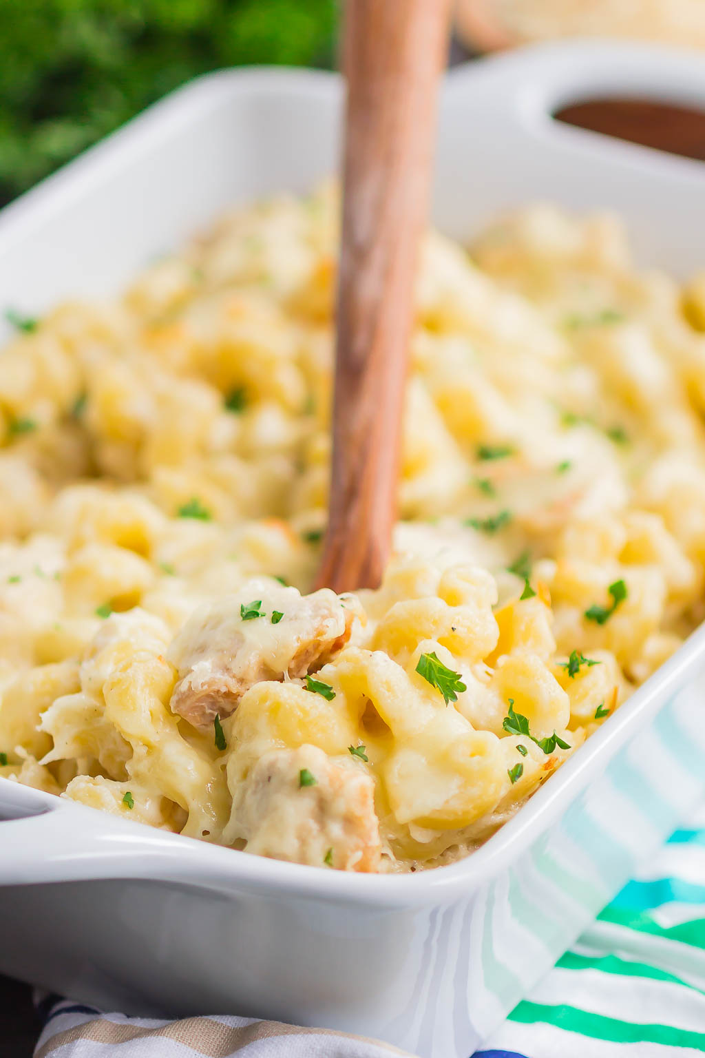 A serving of easy chicken alfredo bake being dug out of a baking dish with a wooden spoon. 