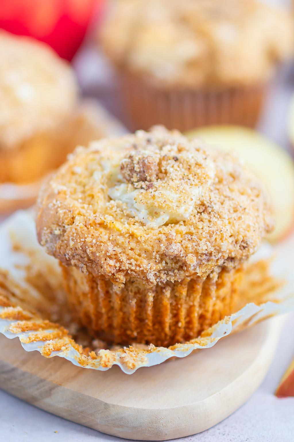 A cream cheese apple streusel muffin with its paper liner pulled down. 