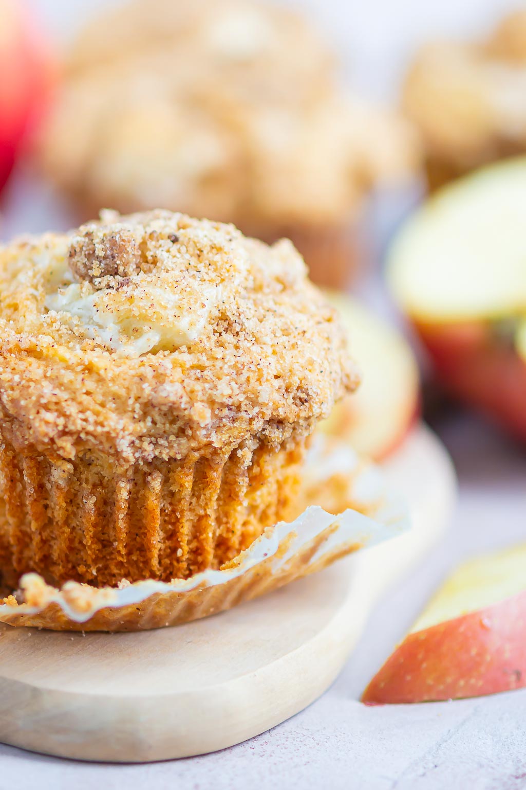Side view of a cream cheese apple cinnamon streusel muffins with its paper liner pulled down. 