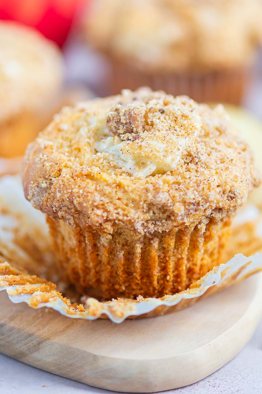 A cream cheese apple cinnamon streusel muffins with its paper liner pulled down. 