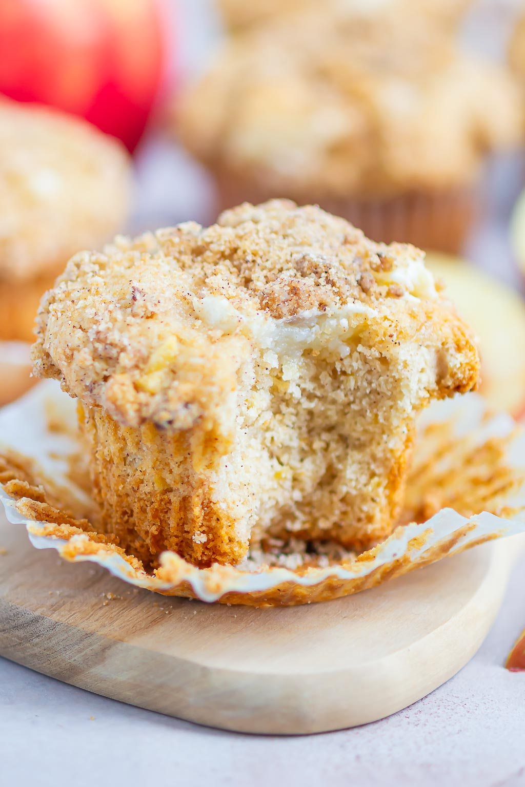 Side view of a apple streusel muffin in a paper liner. A bite has been taken out and the cream cheese filling shows. 