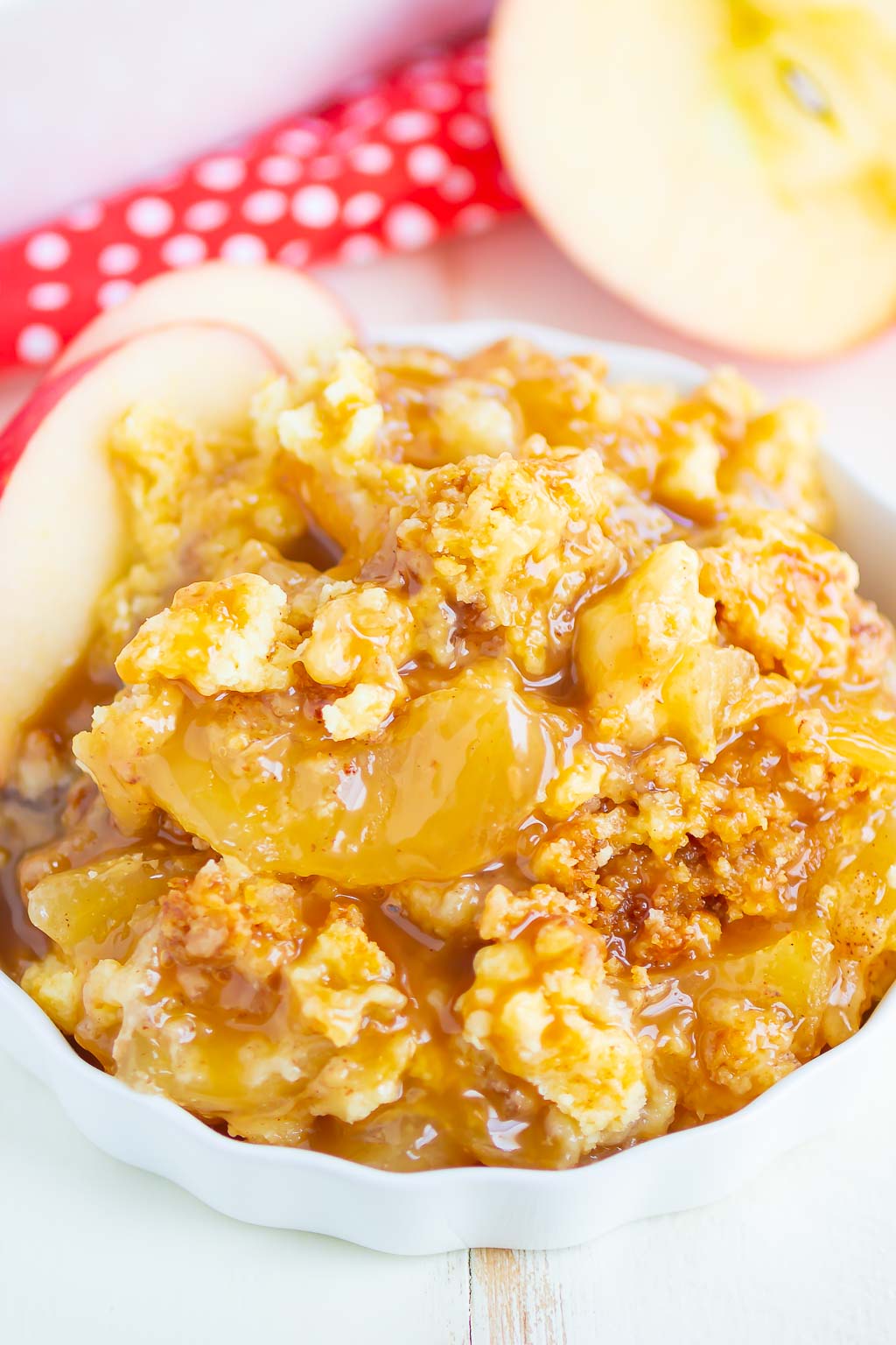 A portion of caramel apple dump cake in a white ramekin. Two apple slices garnish the dish. 