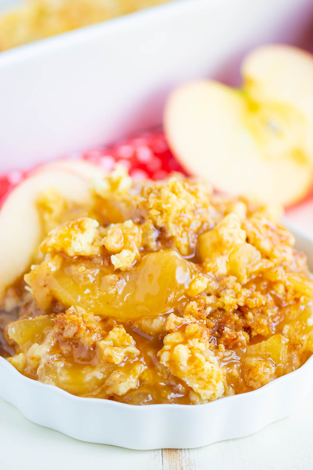 A portion of apple pie filling dump cake in a white ramekin. Two apple slices garnish the dish. 