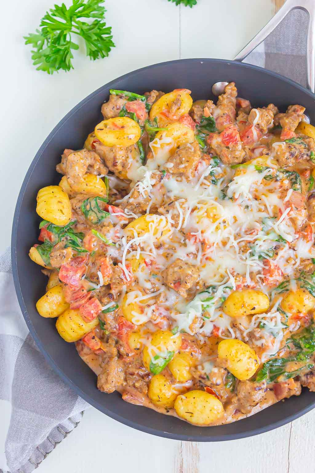 Overhead view of a skillet of Italian sausage gnocchi, topped with shredded mozzarella cheese. 