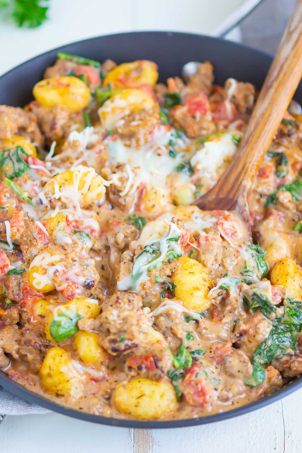 Sausage gnocchi in a skillet. A wooden serving spoon is scooping out a serving. 