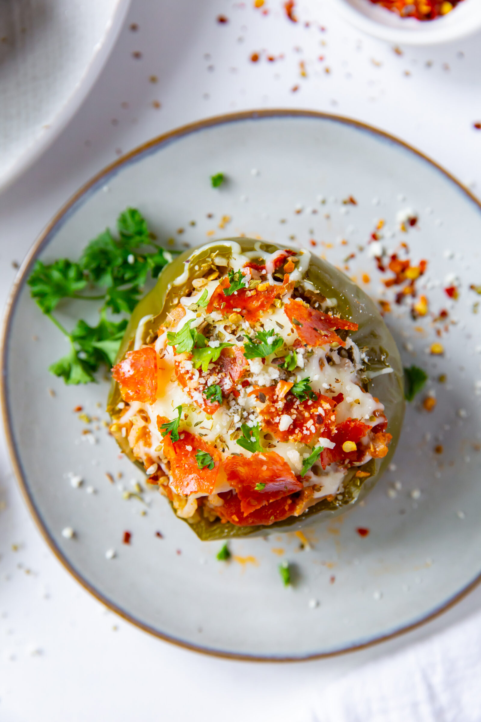 Overhead view of a pizza stuffed pepper on a white plate. 