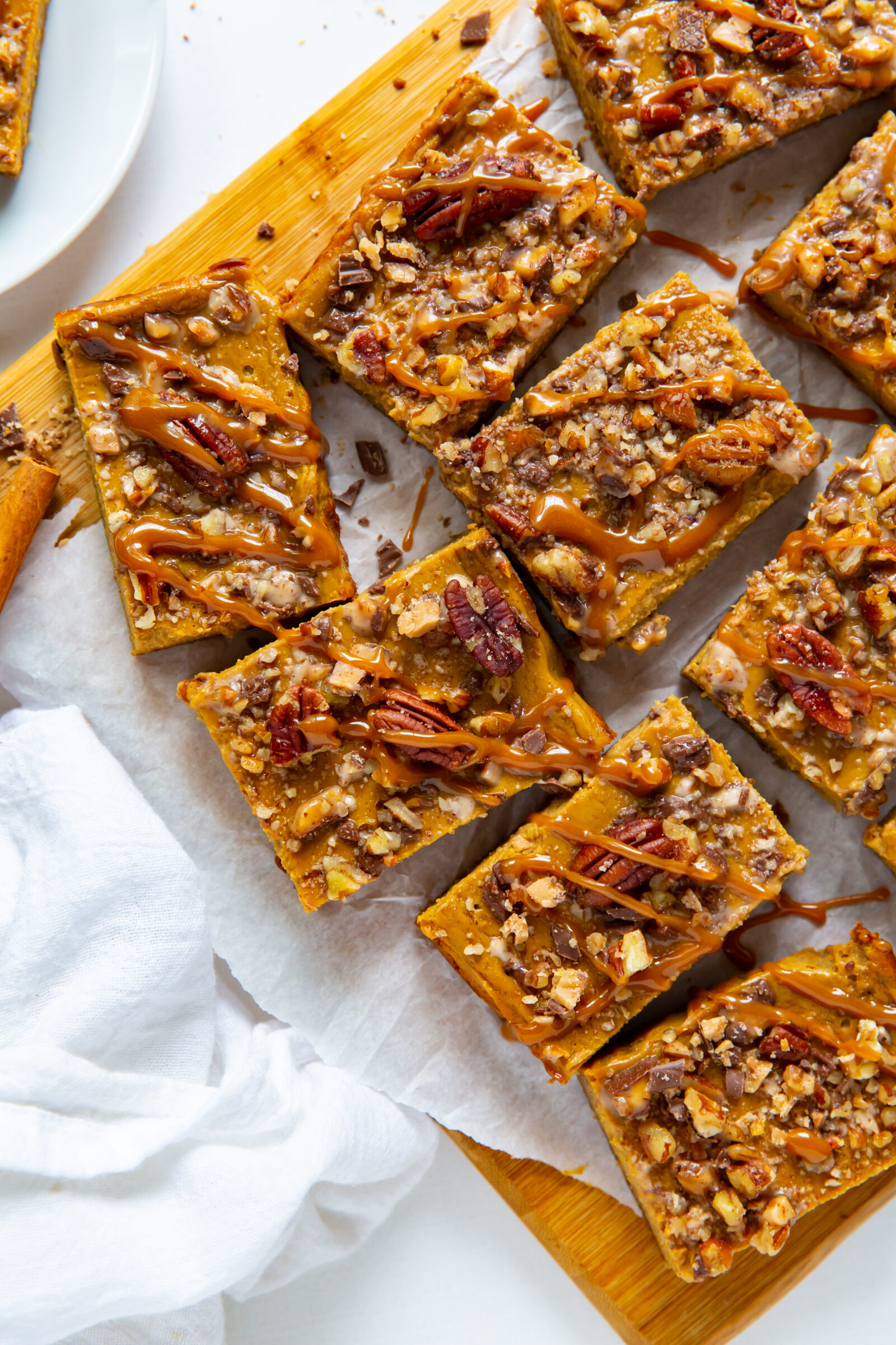 An overhead view of sliced pumpkin pecan bars on a parchment paper-lined wooden board. 