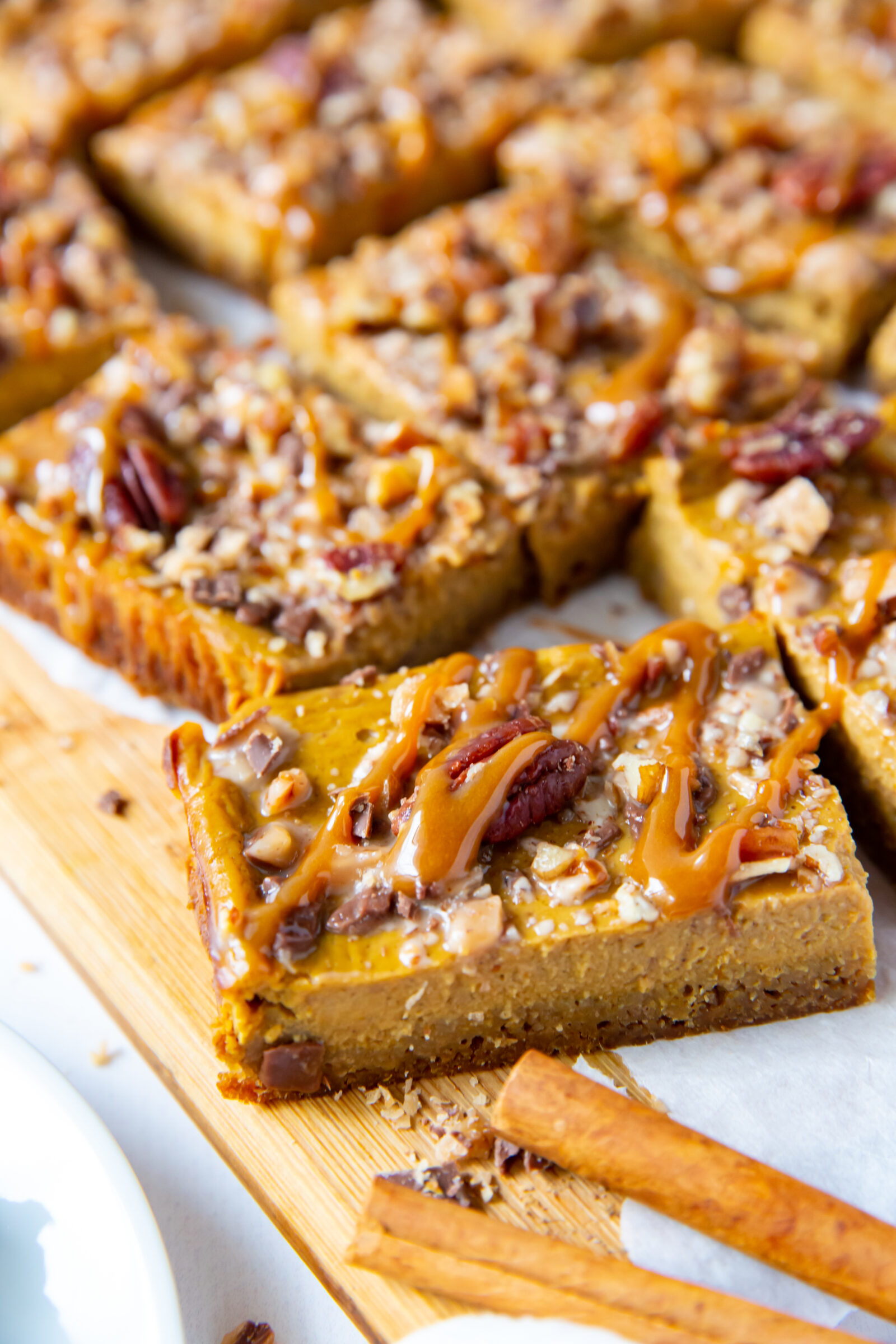 Sliced pumpkin pecan bars on parchment paper, with cinnamon sticks in the foreground. 