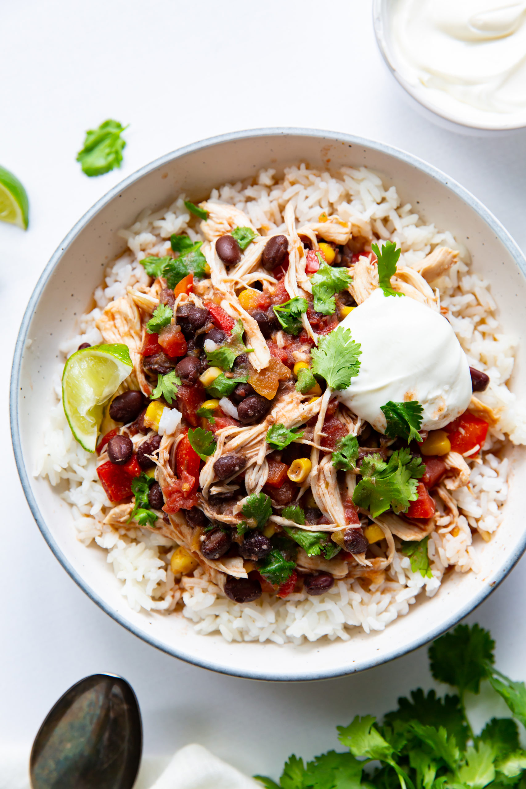 An aerial view of a Southwestern chicken and rice bowl,  garnished with sour cream and fresh cilantro.