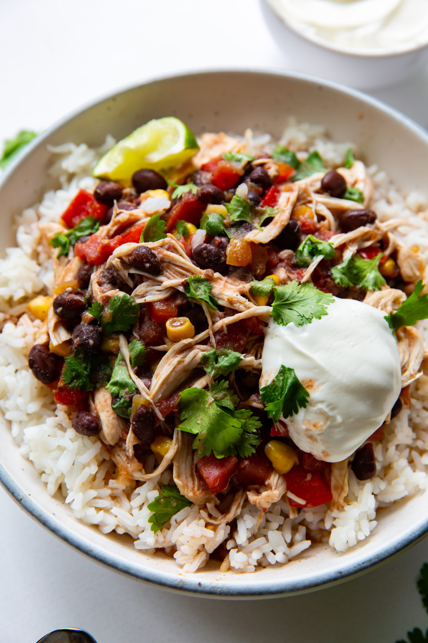 An overhead view of a bowl of southwest chicken and rice, garnished with sour cream and fresh cilantro.