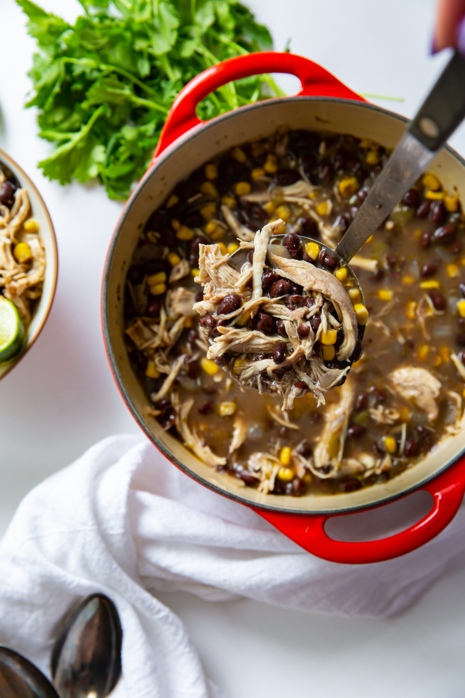 Overhead view of a pot of shredded chicken chili being ladled into bowls. 