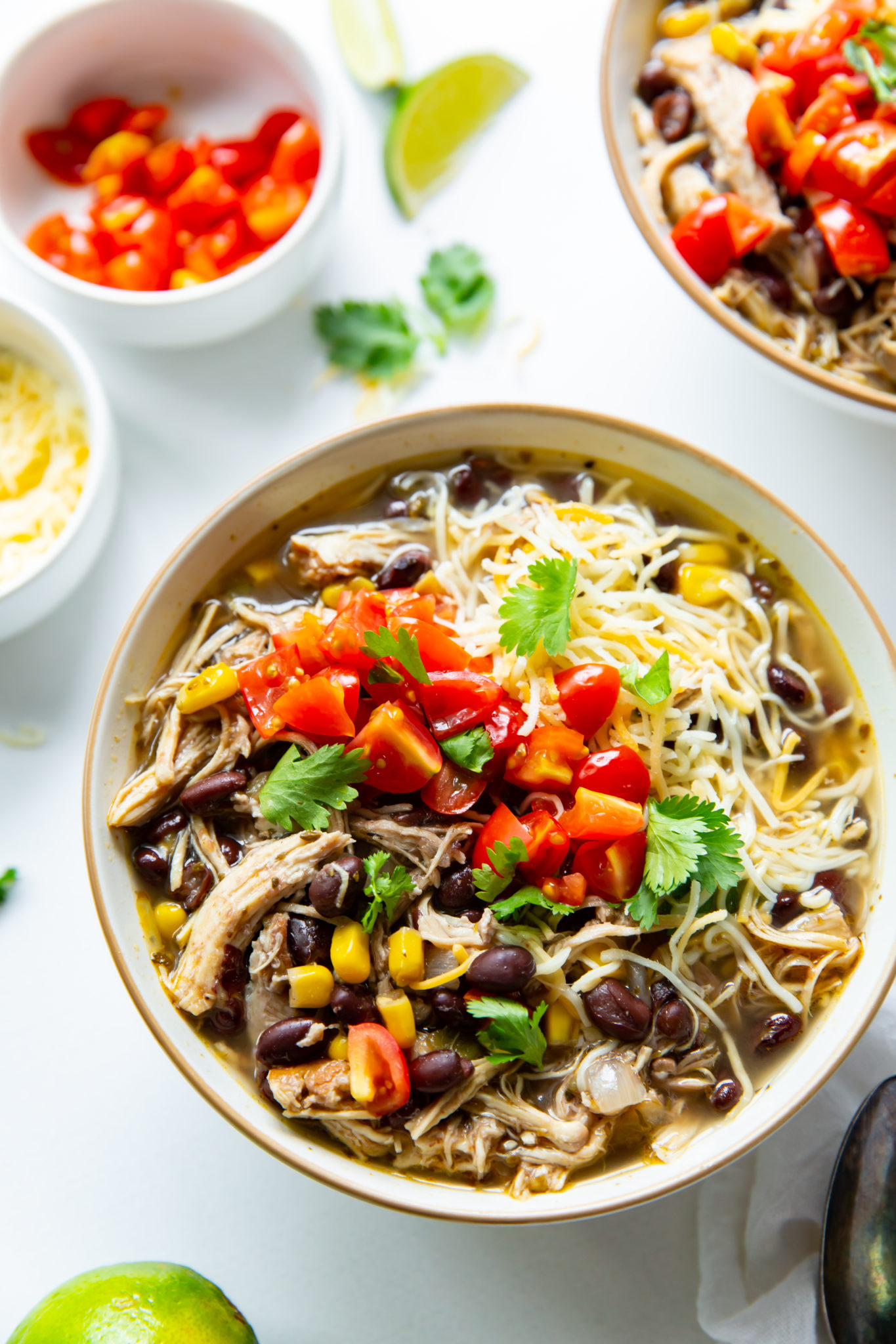 A bowl of chicken chili with beans garnished with cilantro, diced tomatoes, and cheese.