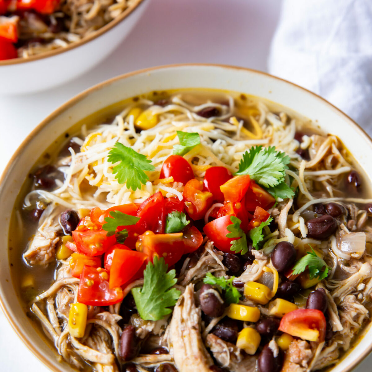 A bowl of black bean chicken chili garnished with cilantro, diced tomatoes, and cheese.