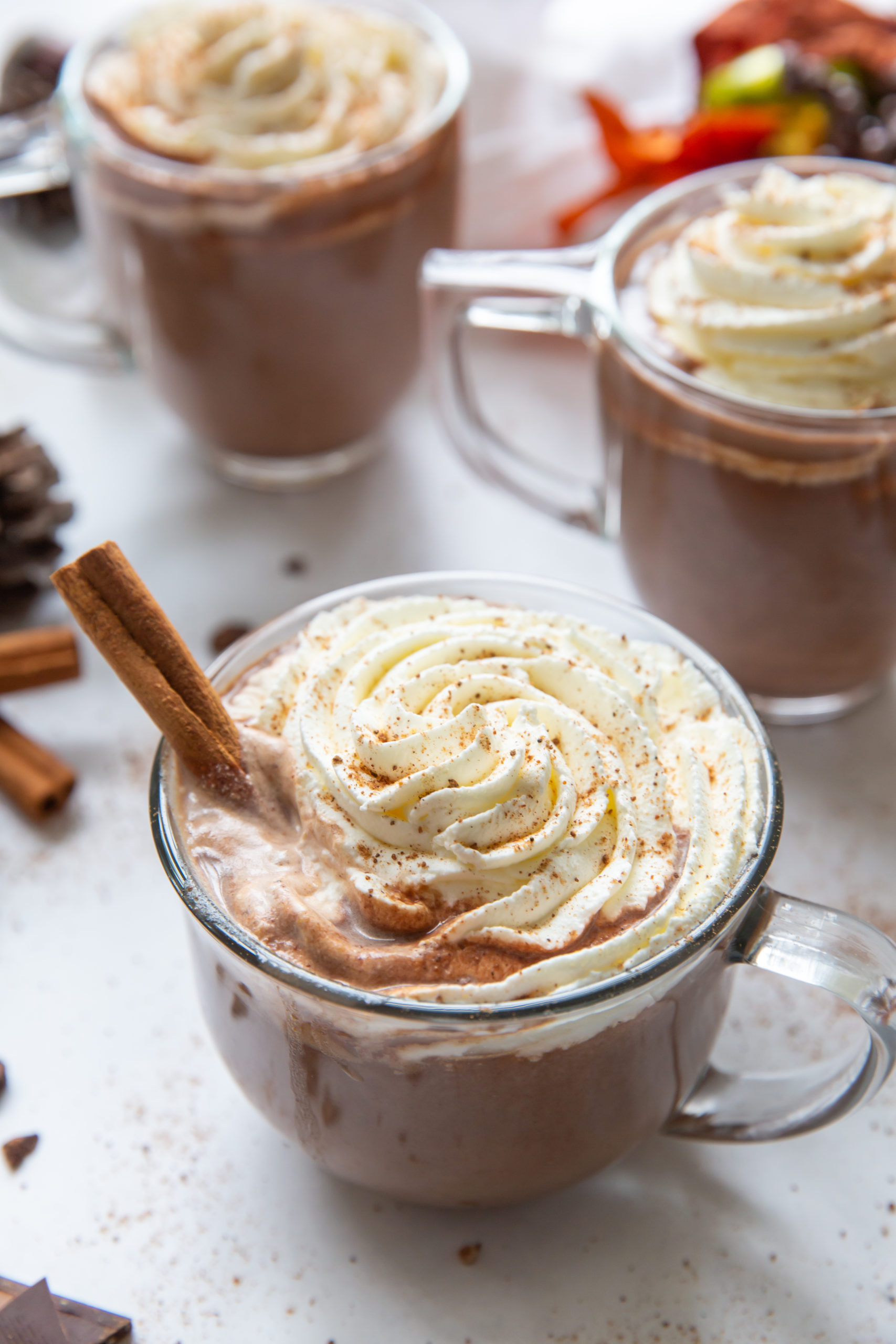 Overhead view of three mugs of pumpkin hot chocolate topped with whipped cream and garnished with a cinnamon stick. 