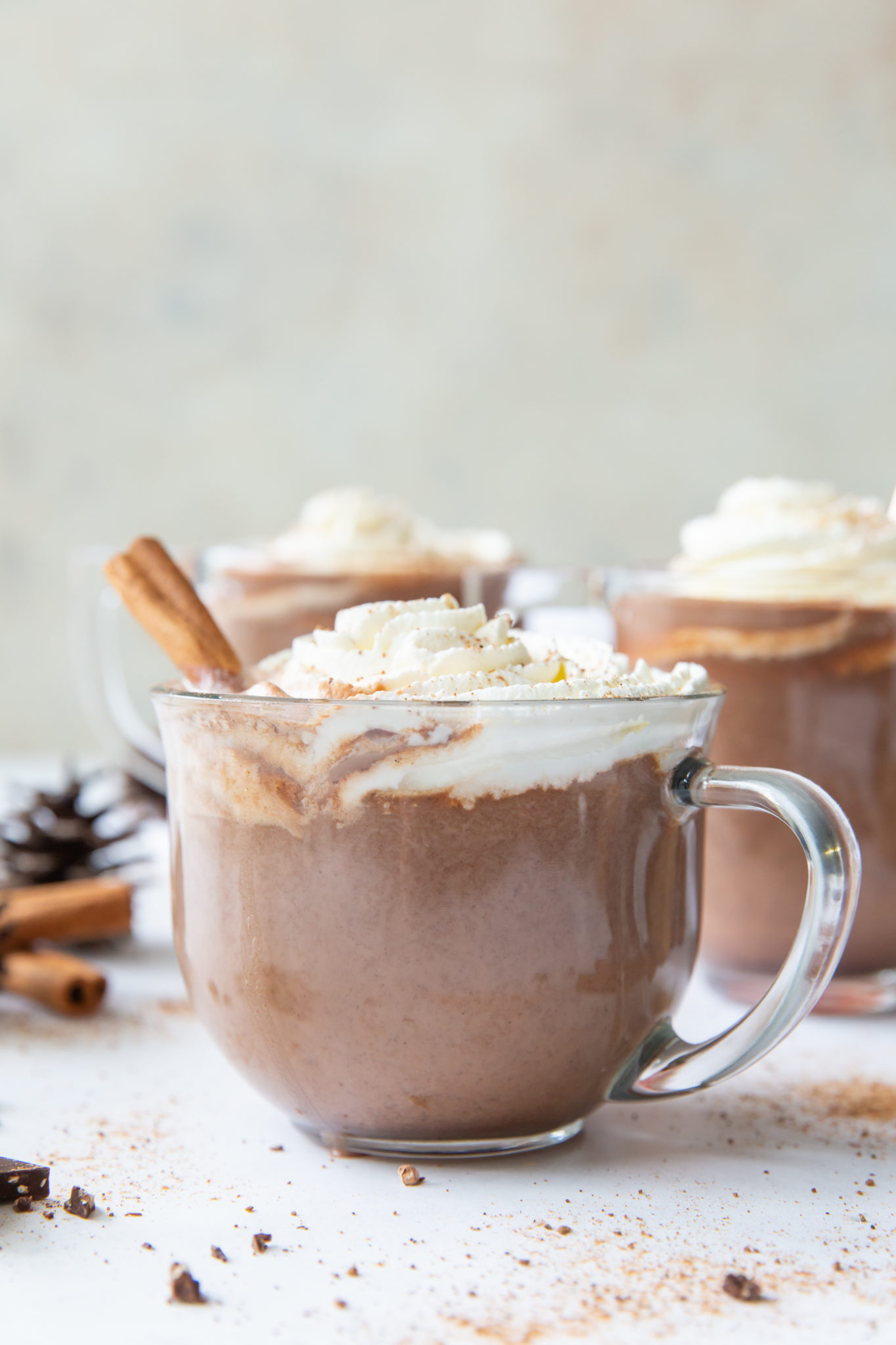 Side view of three mugs of pumpkin hot chocolate topped with whipped cream and garnished with a cinnamon stick.