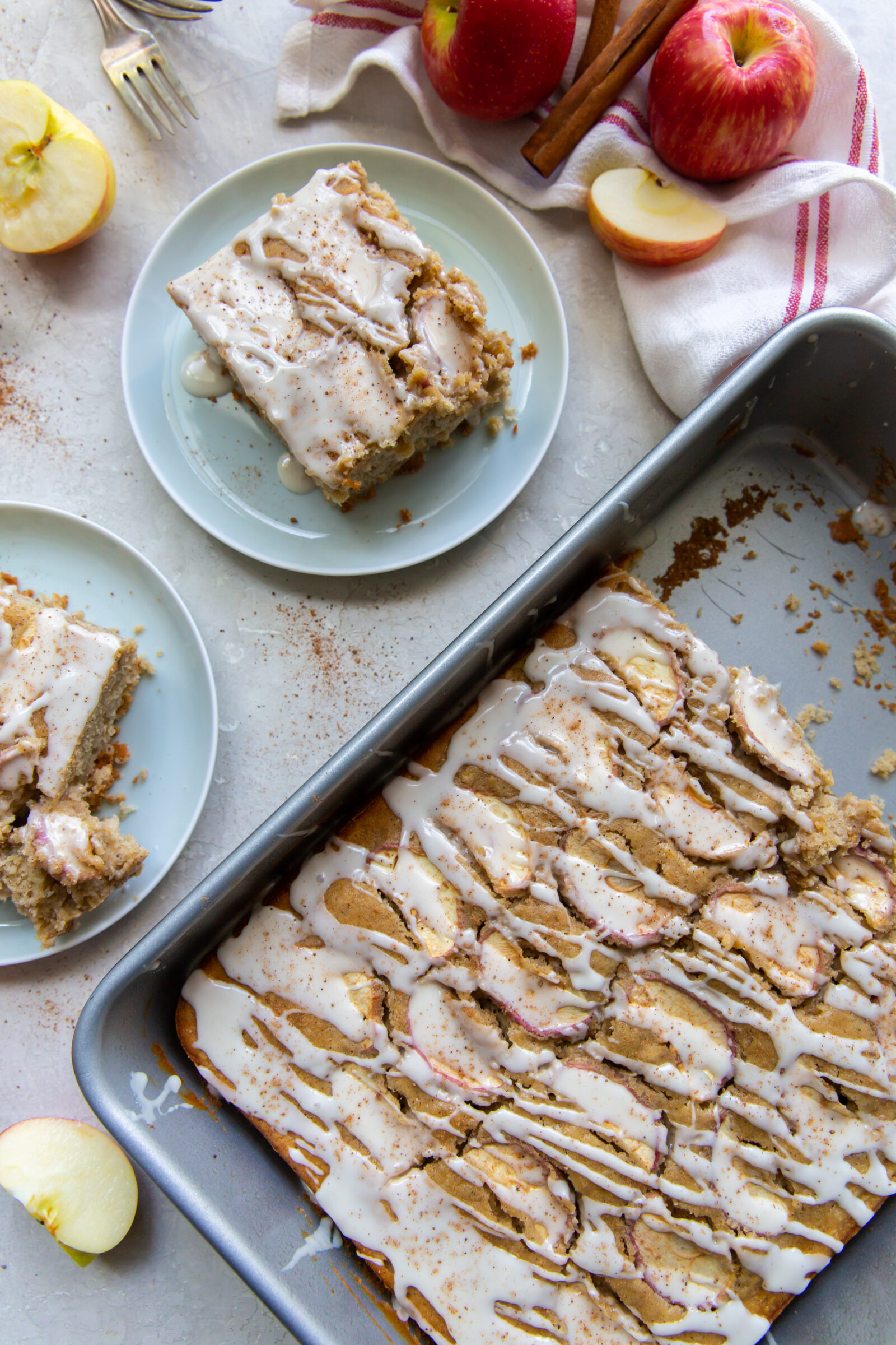 Overhead view of two slices of moist apple cake on blue plates next to a pan of apple cake. 