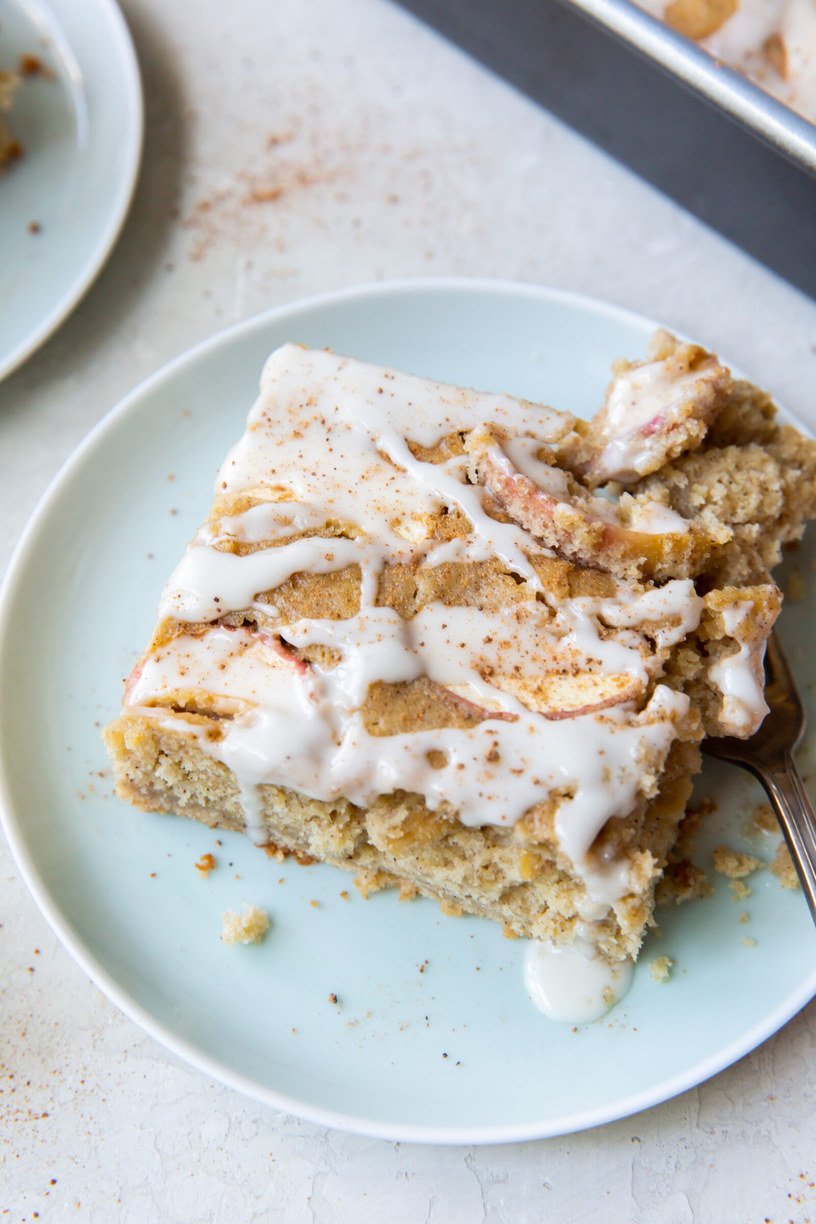 A slice of fresh apple cake topped with glaze on a light blue plate. 