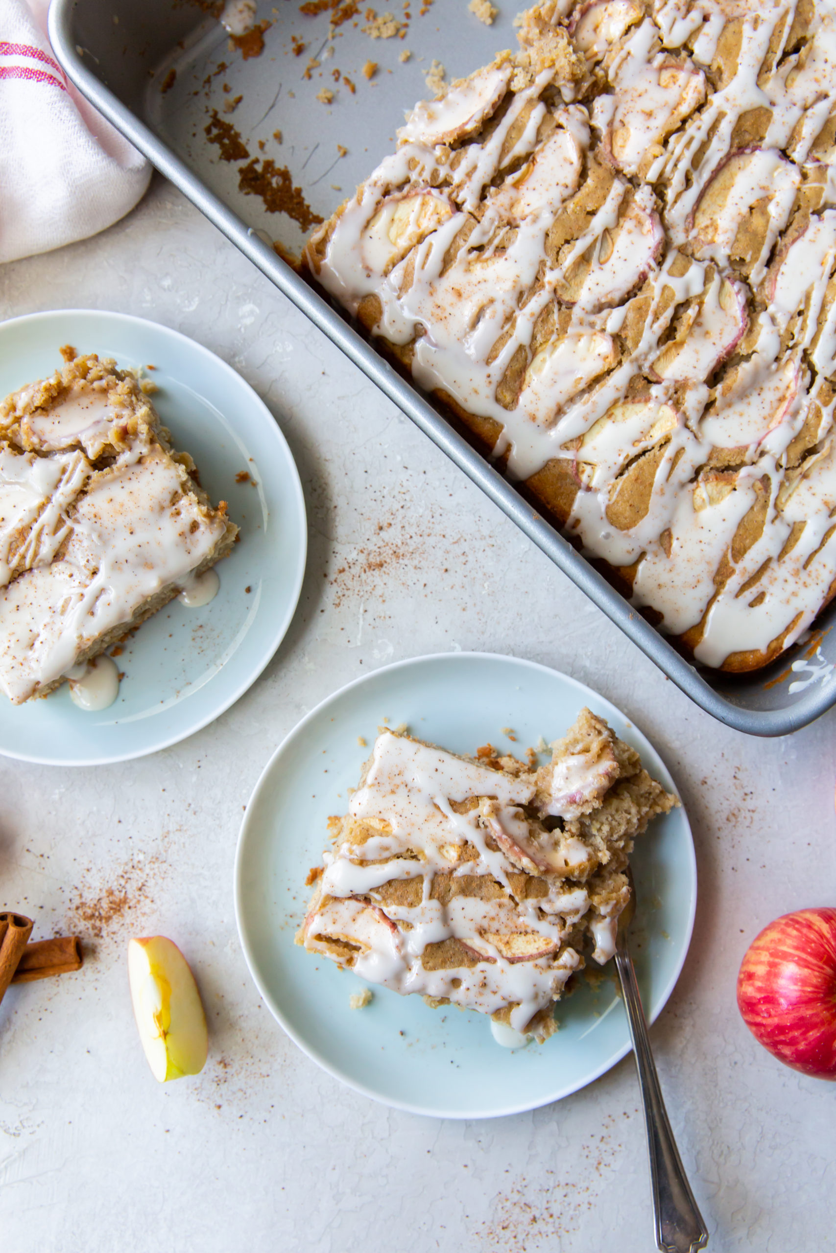 Overhead view of two slices of moist apple cake on blue plates next to a pan of apple cake. 