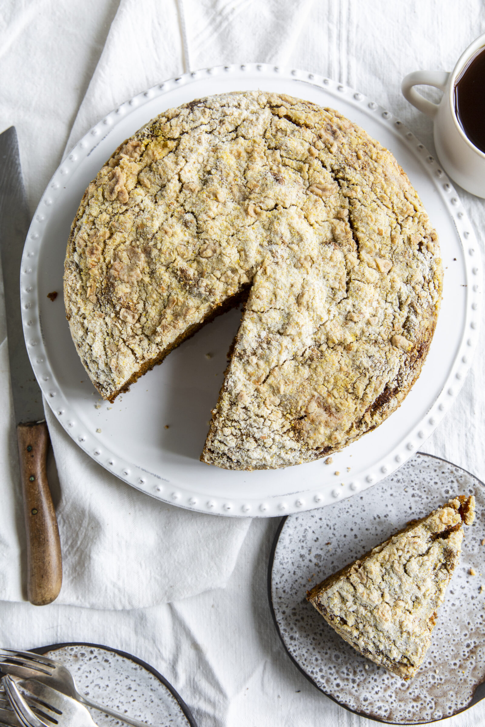 Overhead view of a pumpkin streusel coffee cake on a white platter. A plate with a slice of coffee cake is on the side. 