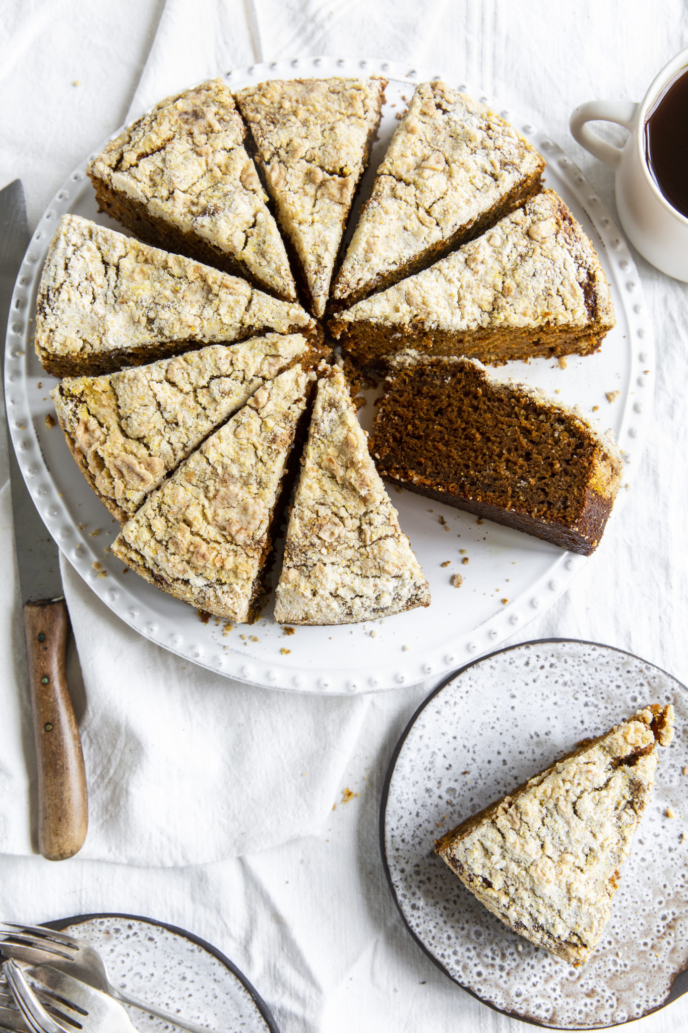 Overhead view of a sliced pumpkin spice coffee cake on a white platter, with a slice on a dessert plate on the side.