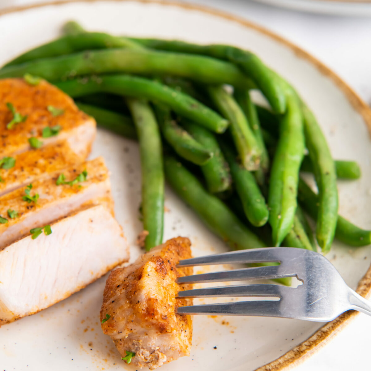 A sliced air fryer pork chop with green beans on a white speckled plate